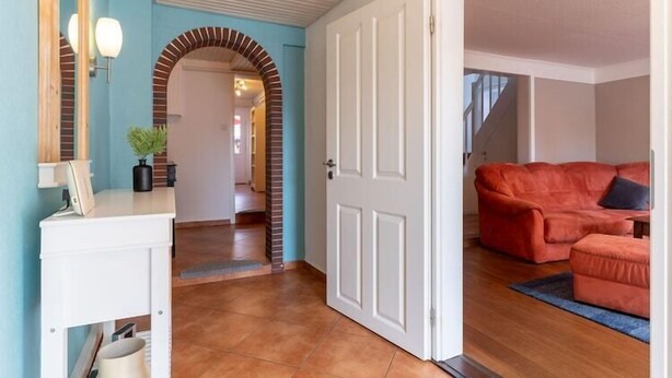 A living room with a red sofa and a small ottoman, a white door, and a blue wall with a brick archway. - Ferienhaus in Tönning (Tönning)