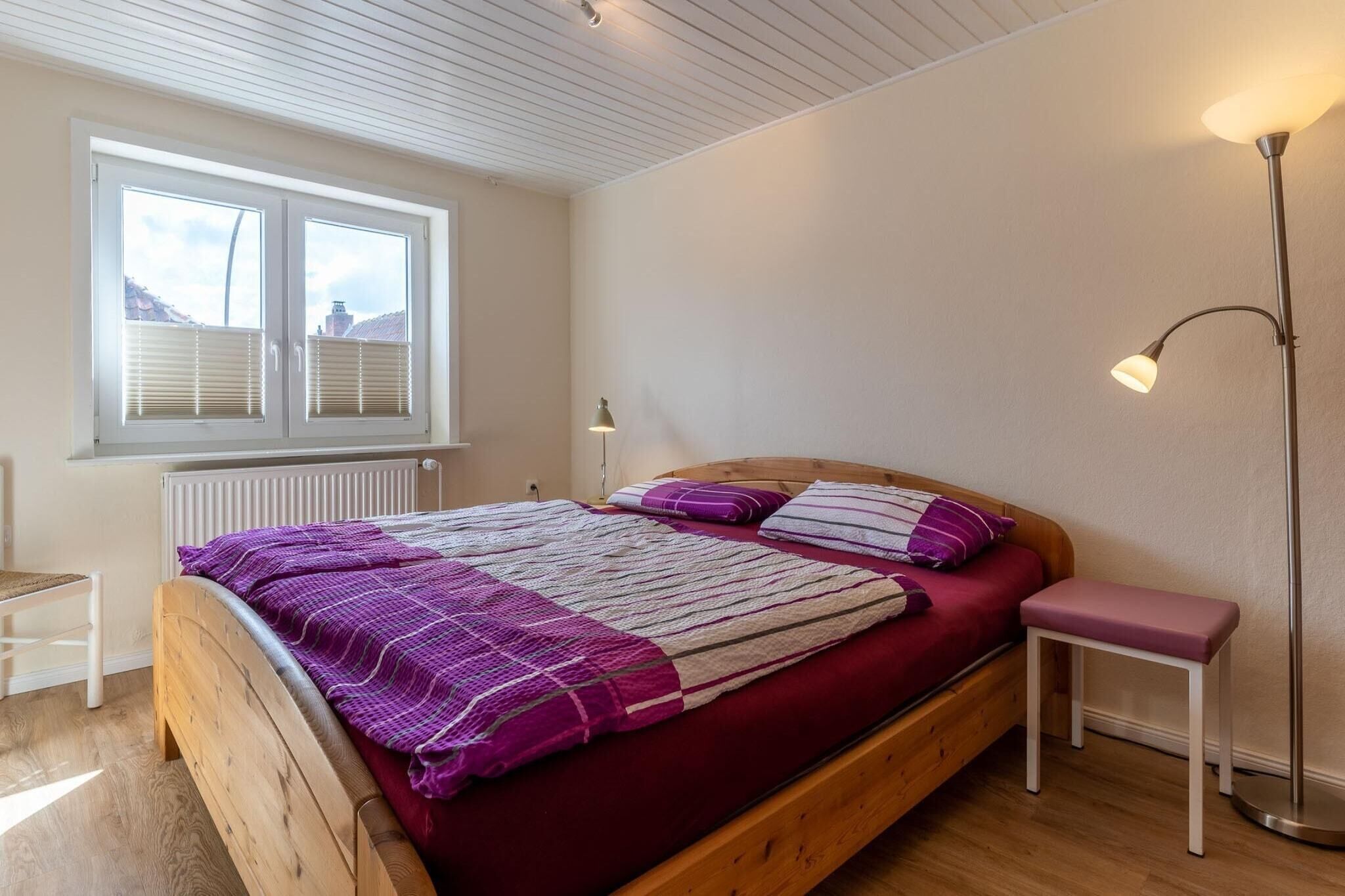A bedroom with a wooden bed, a window with blinds, a bedside table, and a floor lamp.