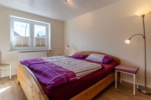 A bedroom with a wooden bed, a window with blinds, a bedside table, and a floor lamp. - Ferienhaus in Tönning (Tönning)