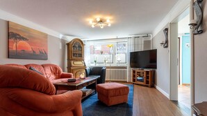 A living room with a sofa, ottoman, wooden coffee table, and a television on a stand. - Ferienhaus in Tönning (Tönning)