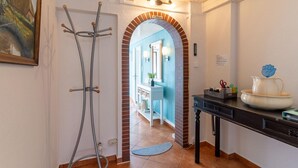 A hallway with a door leading to a bathroom, a coat rack, and a table with a pitcher and a flower vase. - Ferienhaus in Tönning (Tönning)