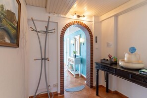 A hallway with a door leading to a bathroom, a coat rack, and a table with a pitcher and a flower vase. - Ferienhaus in Tönning (Tönning)