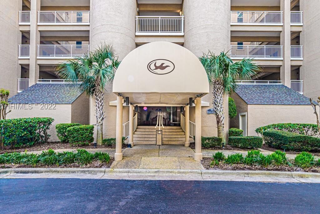 A hotel entrance with a central archway, palm trees, and a multi-story building with balconies.