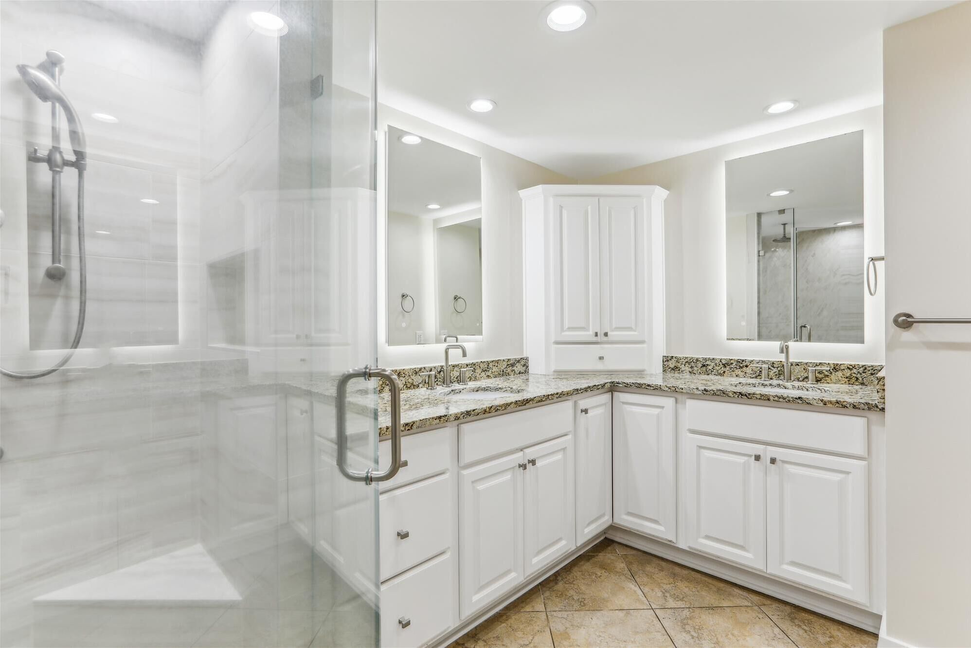 Une salle de bain moderne dotée d’une douche à parois de verre, de meubles blancs, de plans de travail en granit et d’un grand miroir.