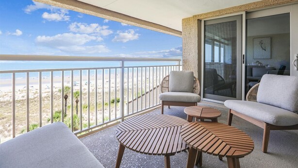 Ein Balkon mit Blick auf den Strand, eine Sitzecke mit einem Sessel und zwei Tischen sowie eine Glastür zum Innenbereich.
