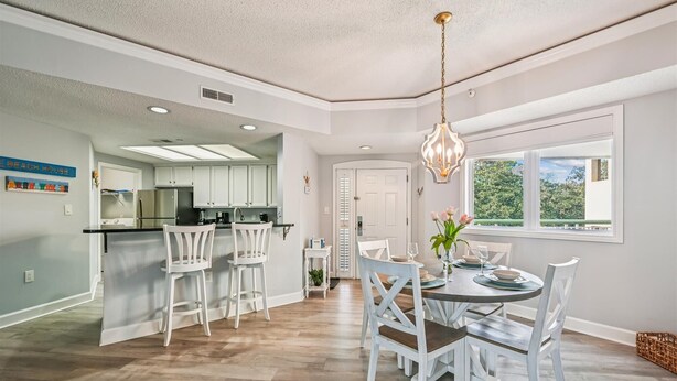 A modern kitchen with white cabinetry, a central island, and a dining area with white chairs and a round table. - Ocean Front Villa w/ Private 4th Floor Balcony (Hilton Head Island)