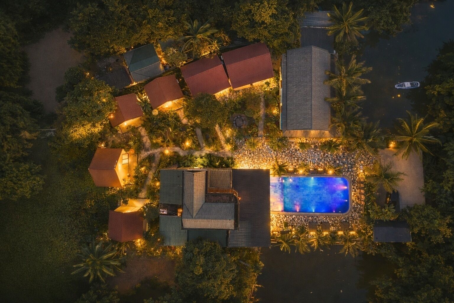 An aerial view of a resort with multiple buildings, a swimming pool, and surrounding palm trees.