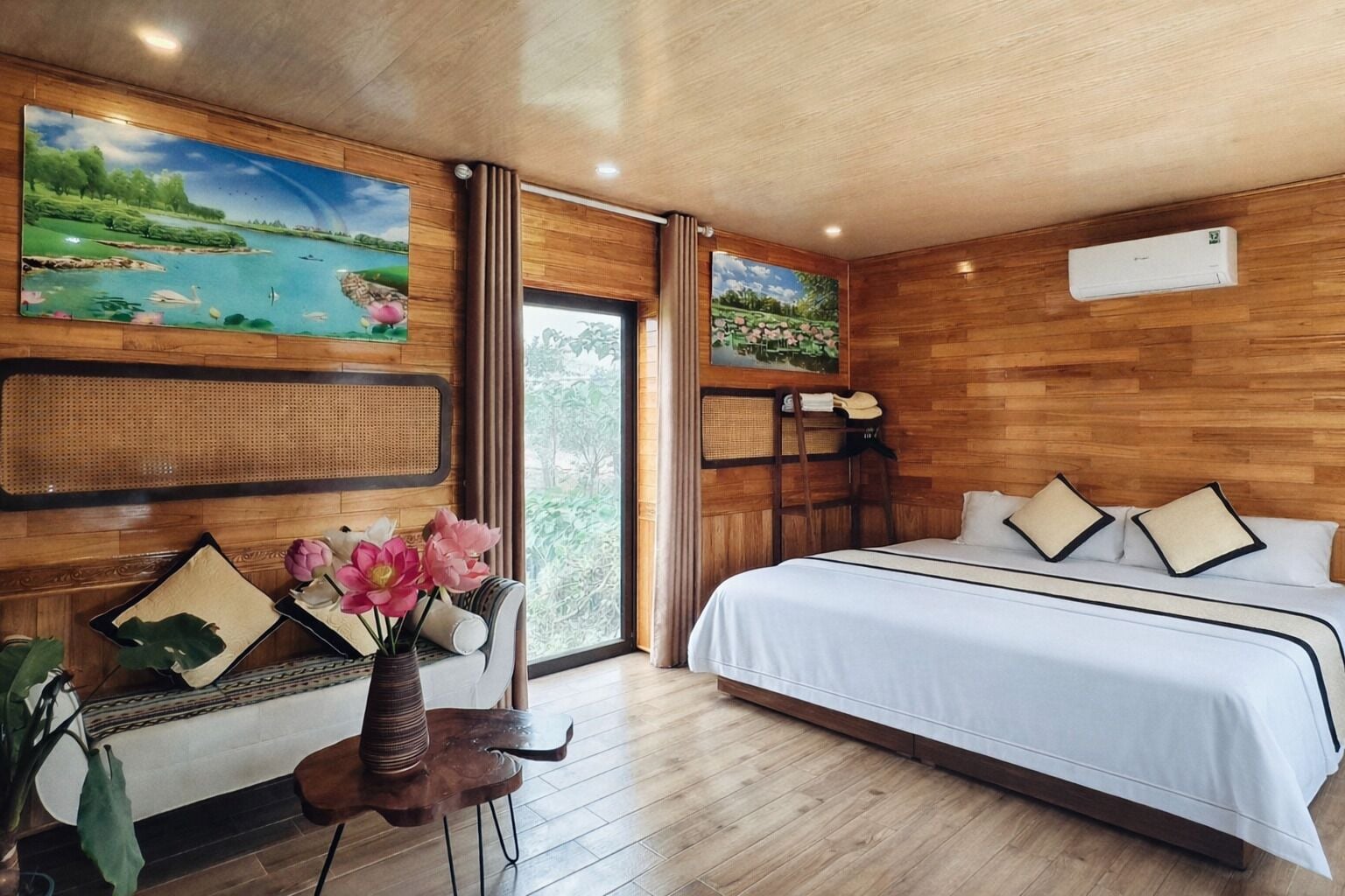 A bedroom with a large bed, a chair, a small table with flowers, and two wall-mounted paintings.