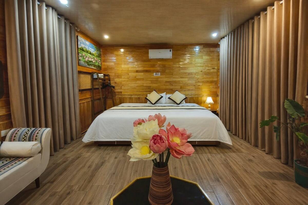 Une chambre d’hôtel avec un mur en bois, un lit avec une literie blanche, une table de chevet avec une lampe et un vase rempli de fleurs.