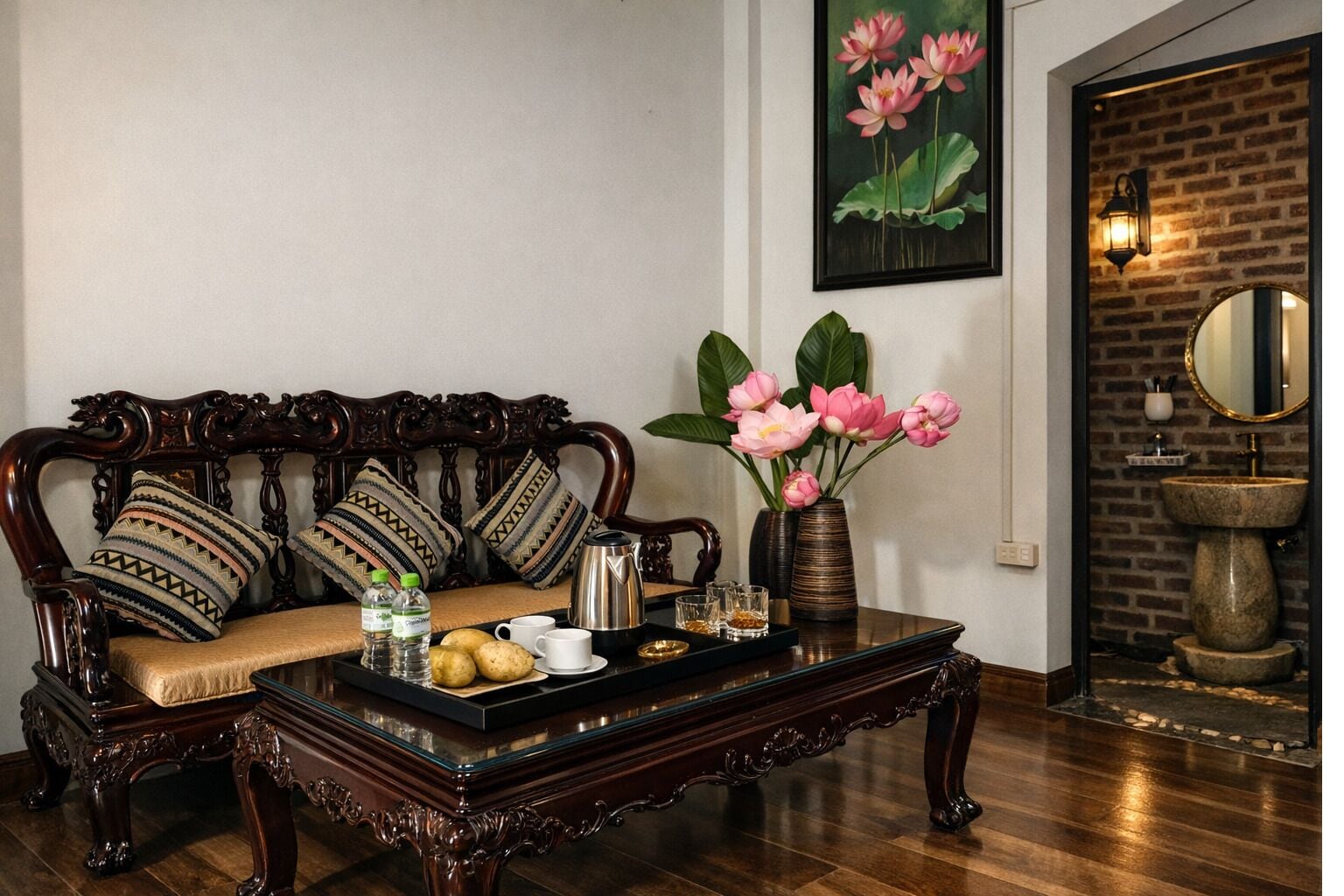A traditional sofa with patterned cushions, a coffee table with drinks and snacks, a vase with flowers, and a brick wall with a mirror and light fixture.