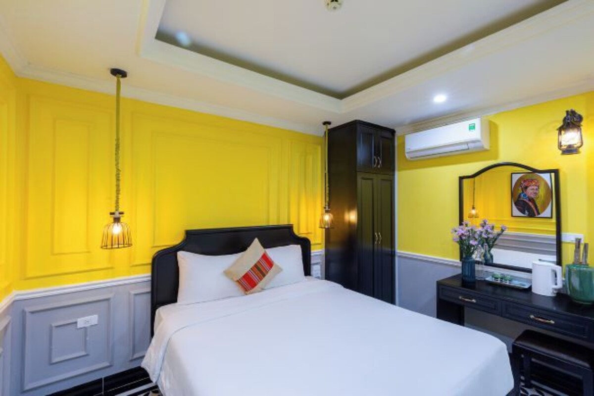 A hotel room with a bed, a dresser, an air conditioning unit, and a wall-mounted lamp.