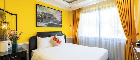 A hotel room with a bed, a painting, a vase with flowers, and a window with curtains.