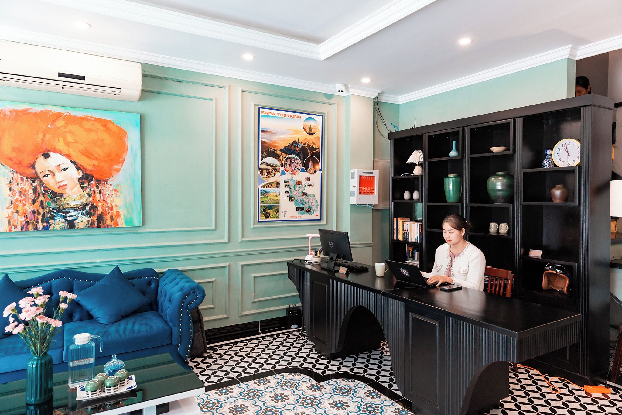 A reception desk with a computer, a blue sofa with decorative pillows, and a wall with a large painting and a poster.