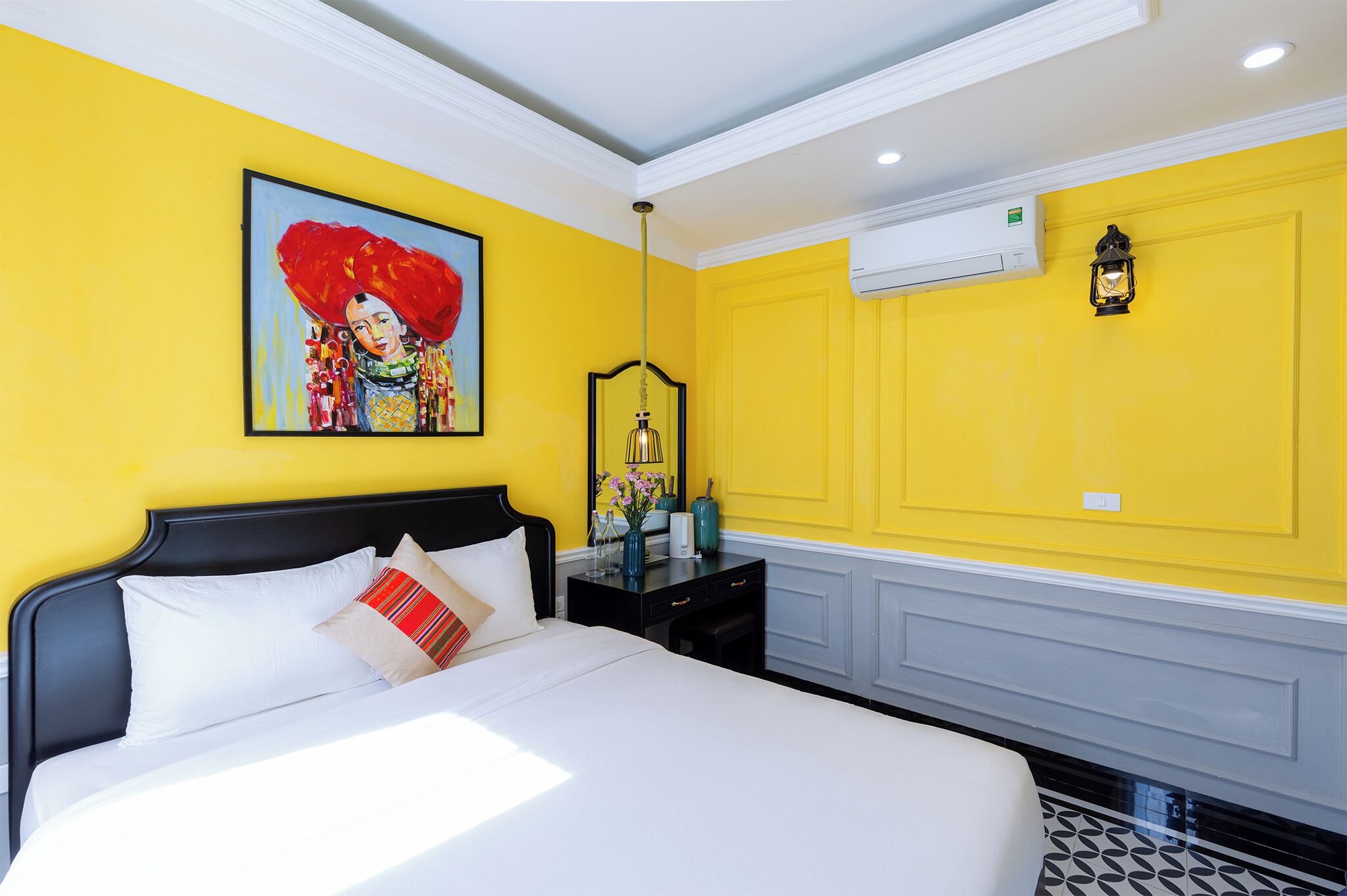 A hotel room with a yellow wall, a black headboard, and a bed with white bedding.
