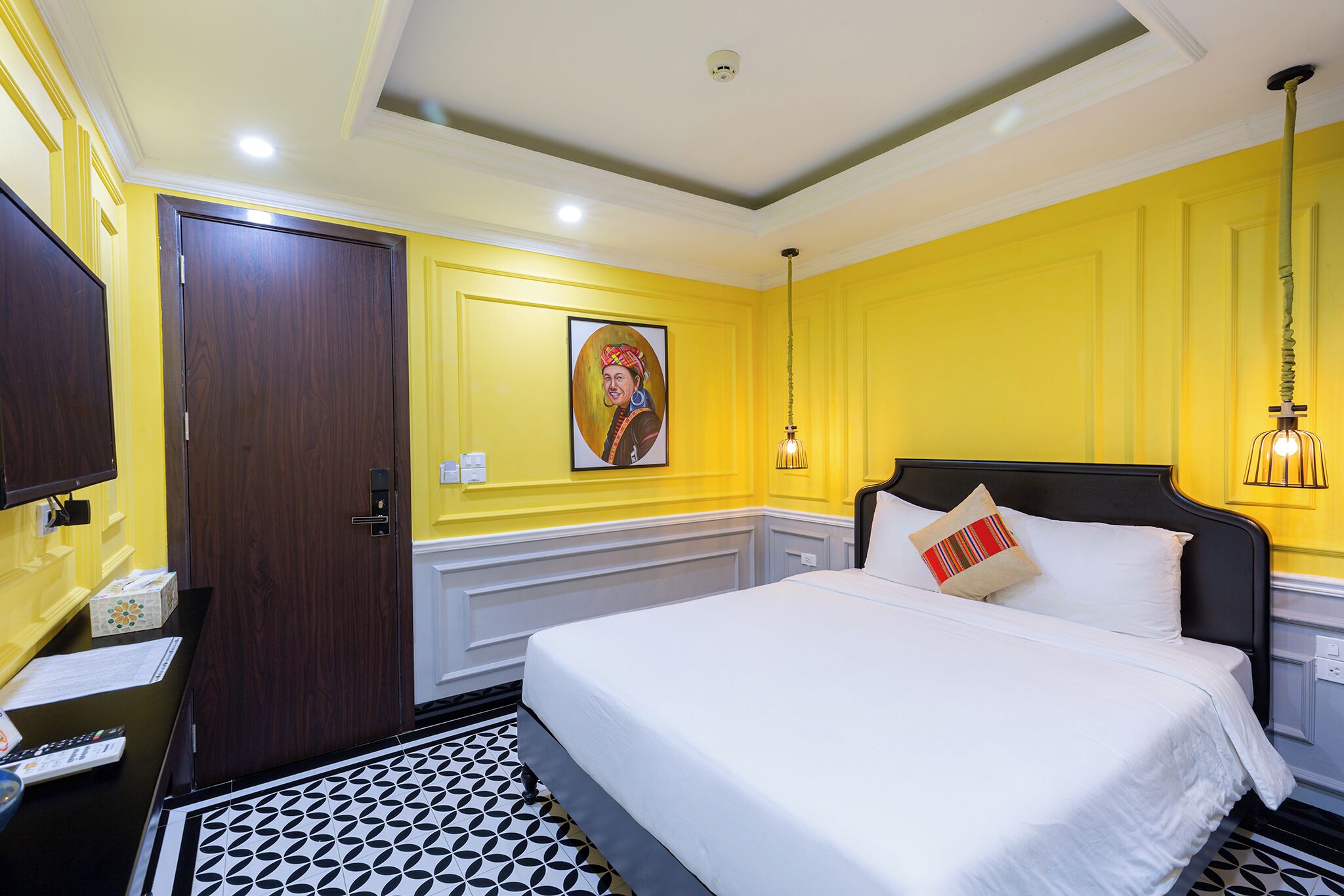A hotel room with a bed, a desk, a chair, a door, and a painting on the wall.