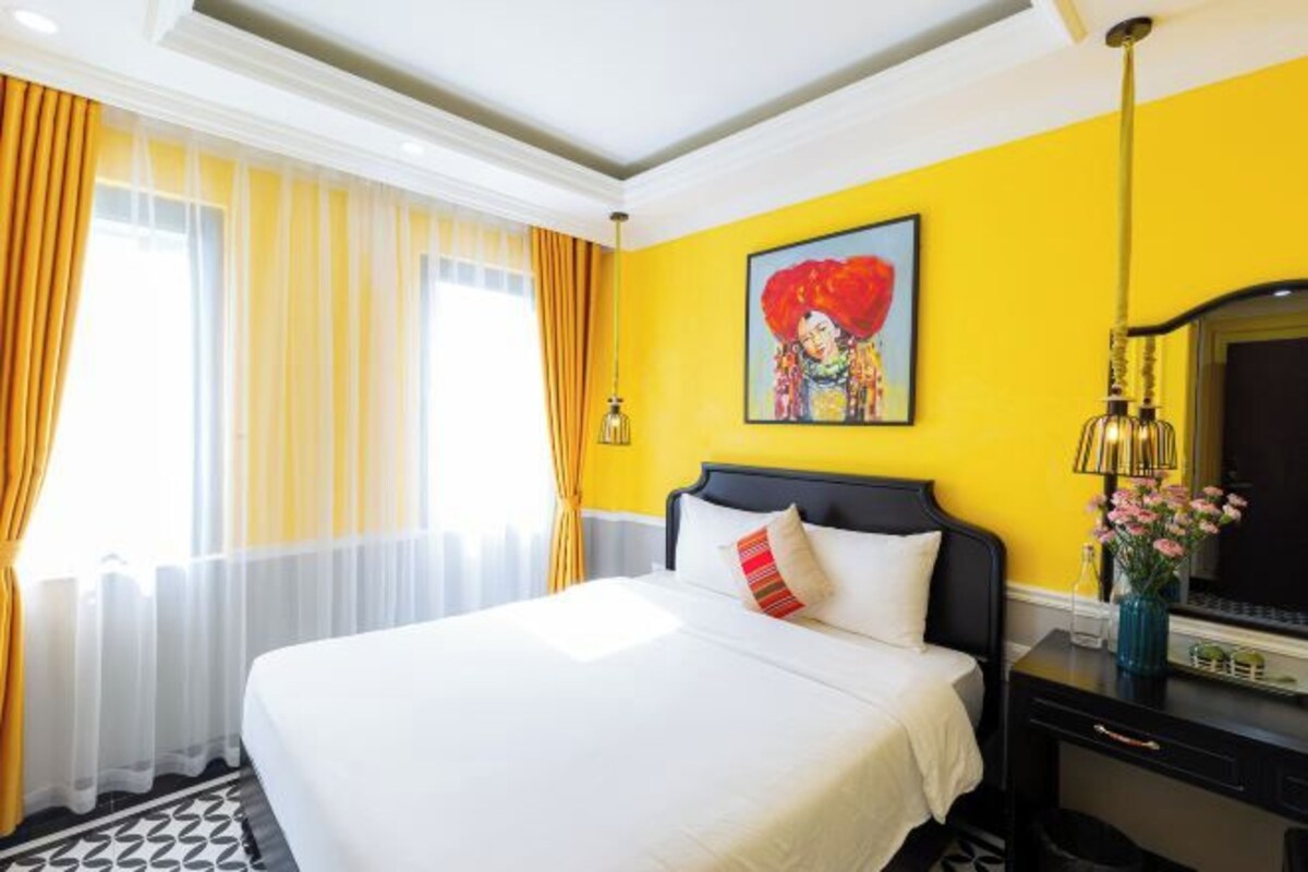 A hotel room with a large bed, yellow walls, and a painting on the wall.