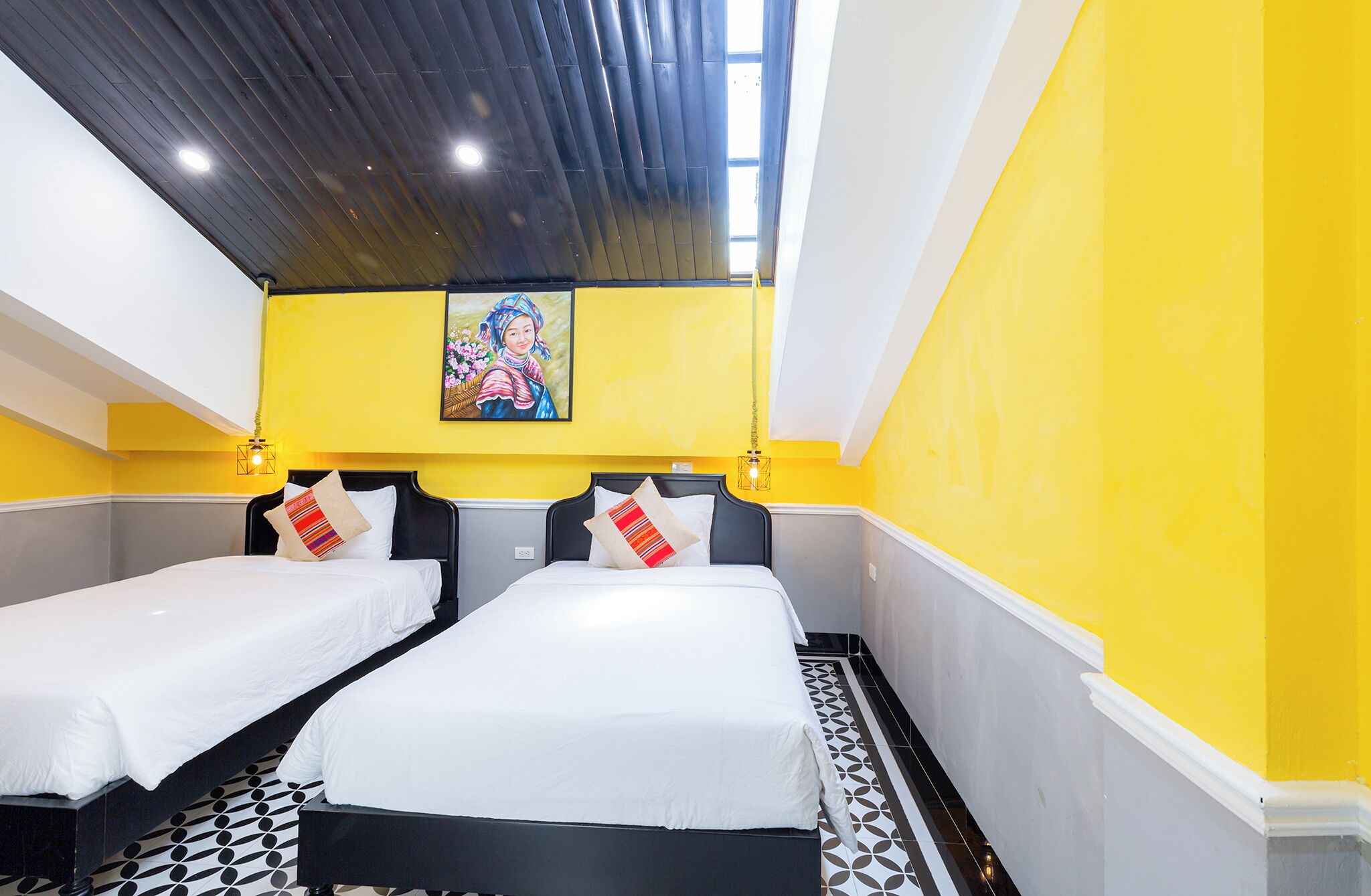 A hotel room with two beds, yellow walls, a black ceiling, and a painting above the beds.