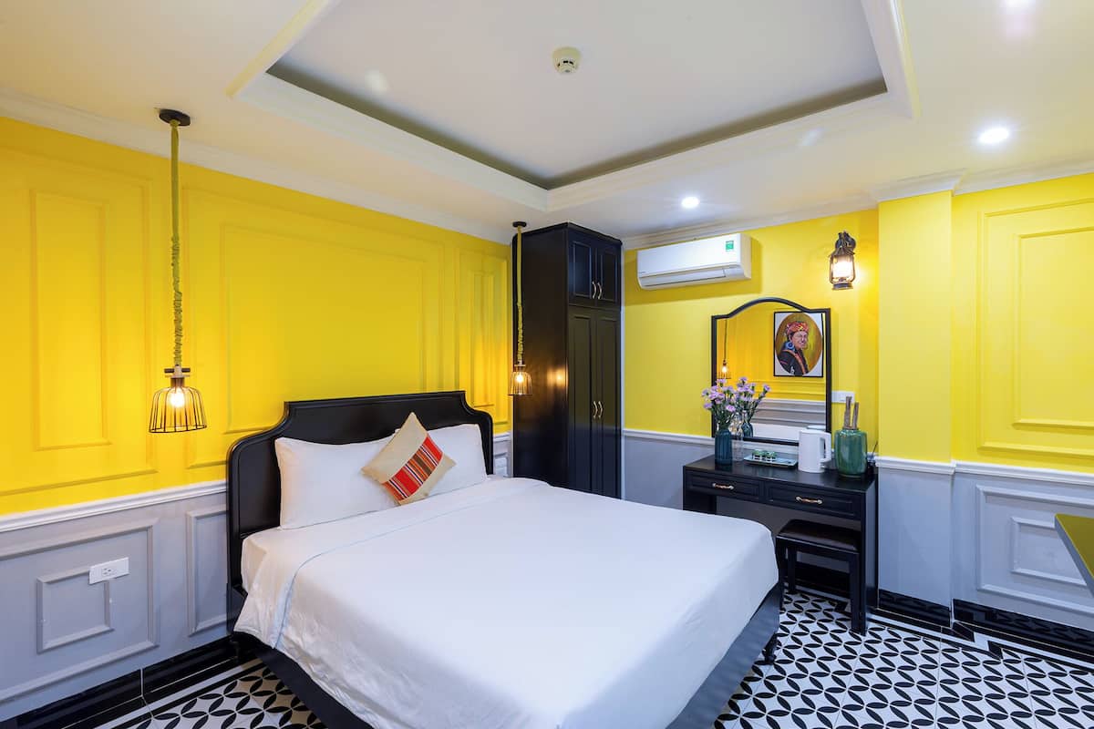 Una habitación de hotel con una cama, un escritorio, un equipo de aire acondicionado y una lámpara fijada a la pared.