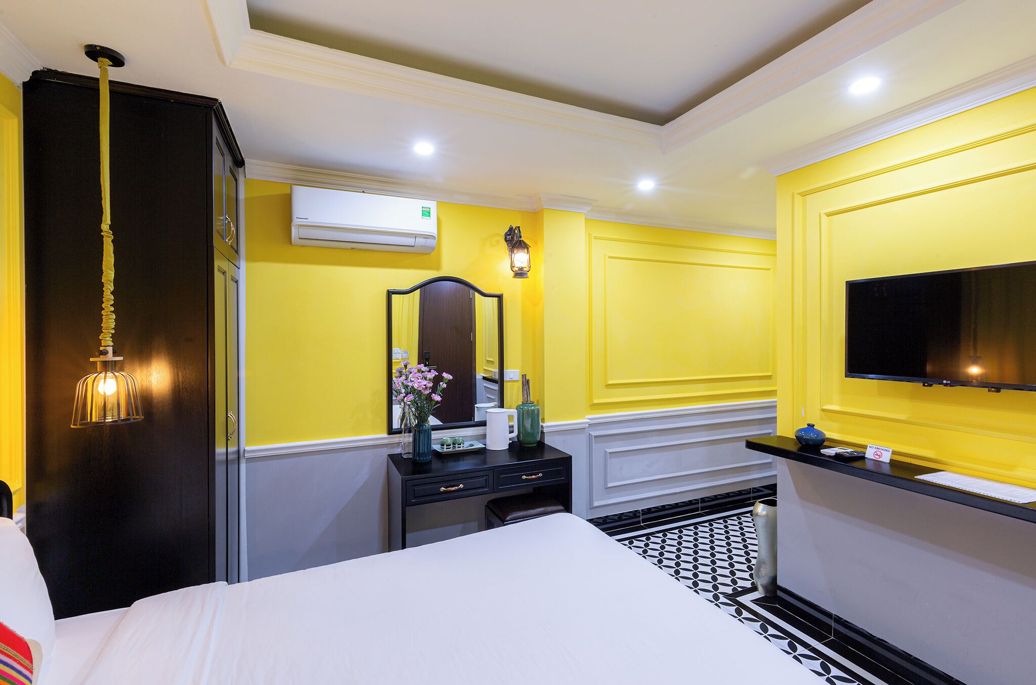 Habitación de hotel con cama, cómoda, espejo, televisión y aire acondicionado.