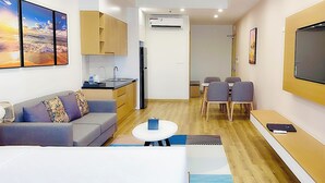 Een moderne woonkamer met een bank, een eethoek met stoelen, een aan de muur bevestigde televisie en een keuken met kasten en een airconditioning.