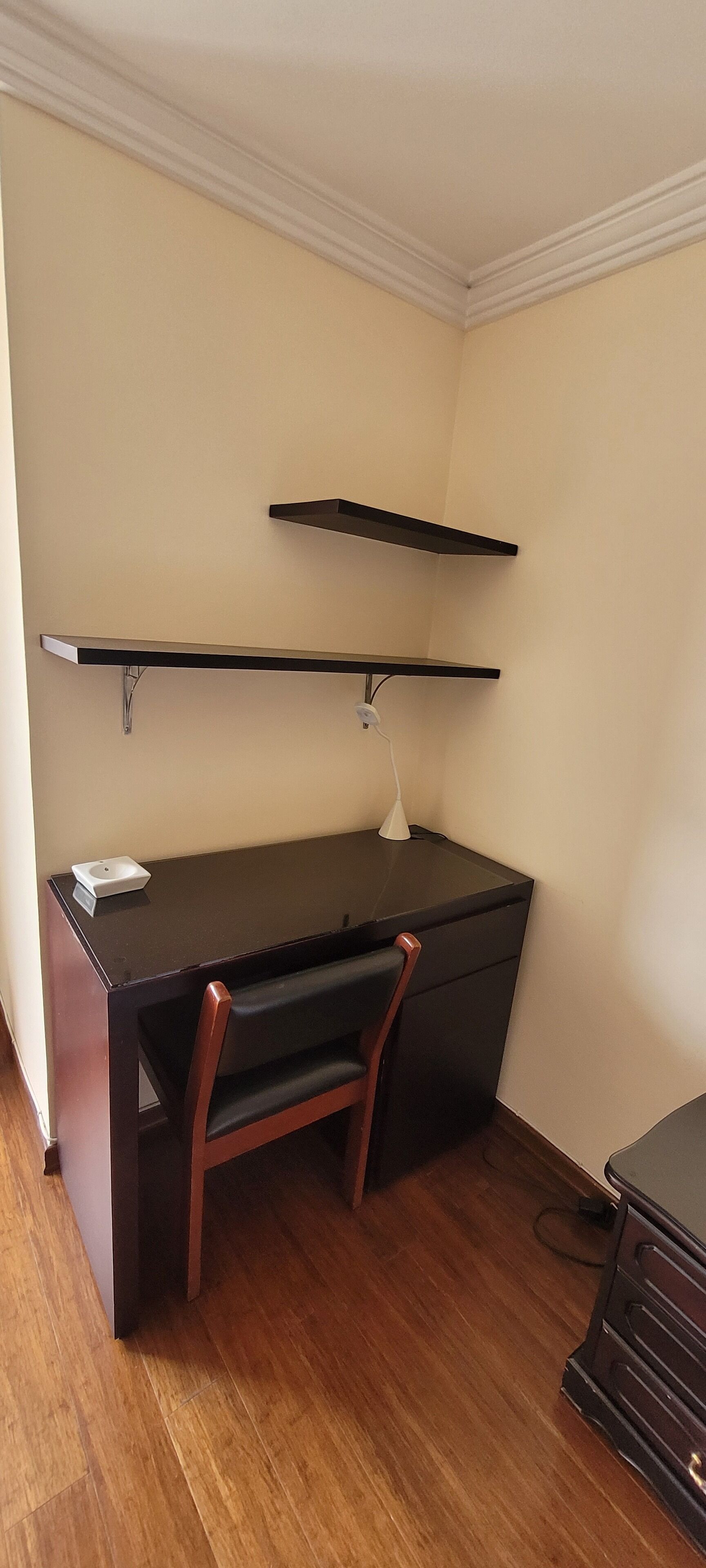 A compact office space with a desk, chair, and two wall-mounted shelves.