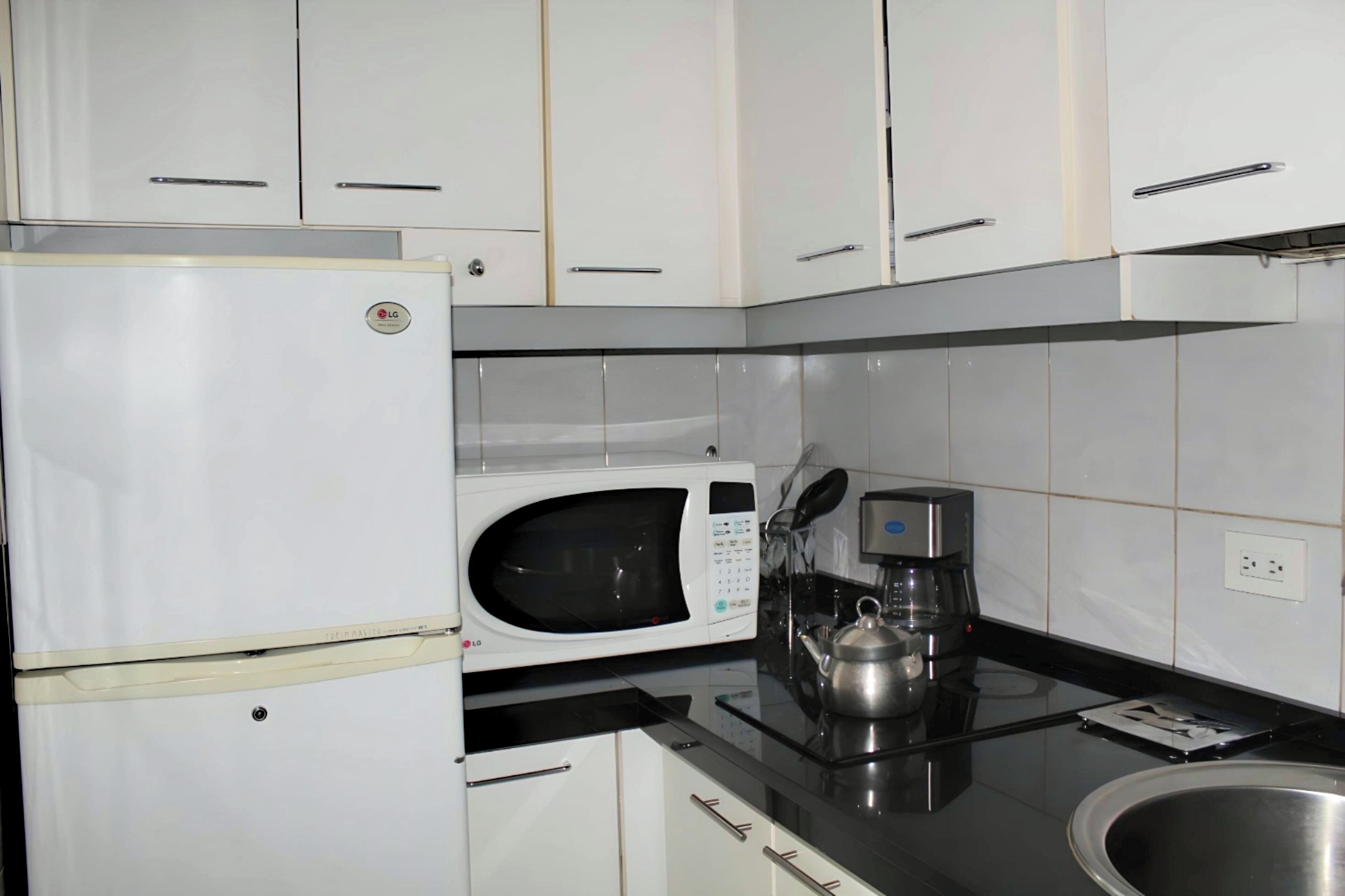 A kitchen with white cabinets, a white refrigerator, a microwave, a coffee maker, and a sink.