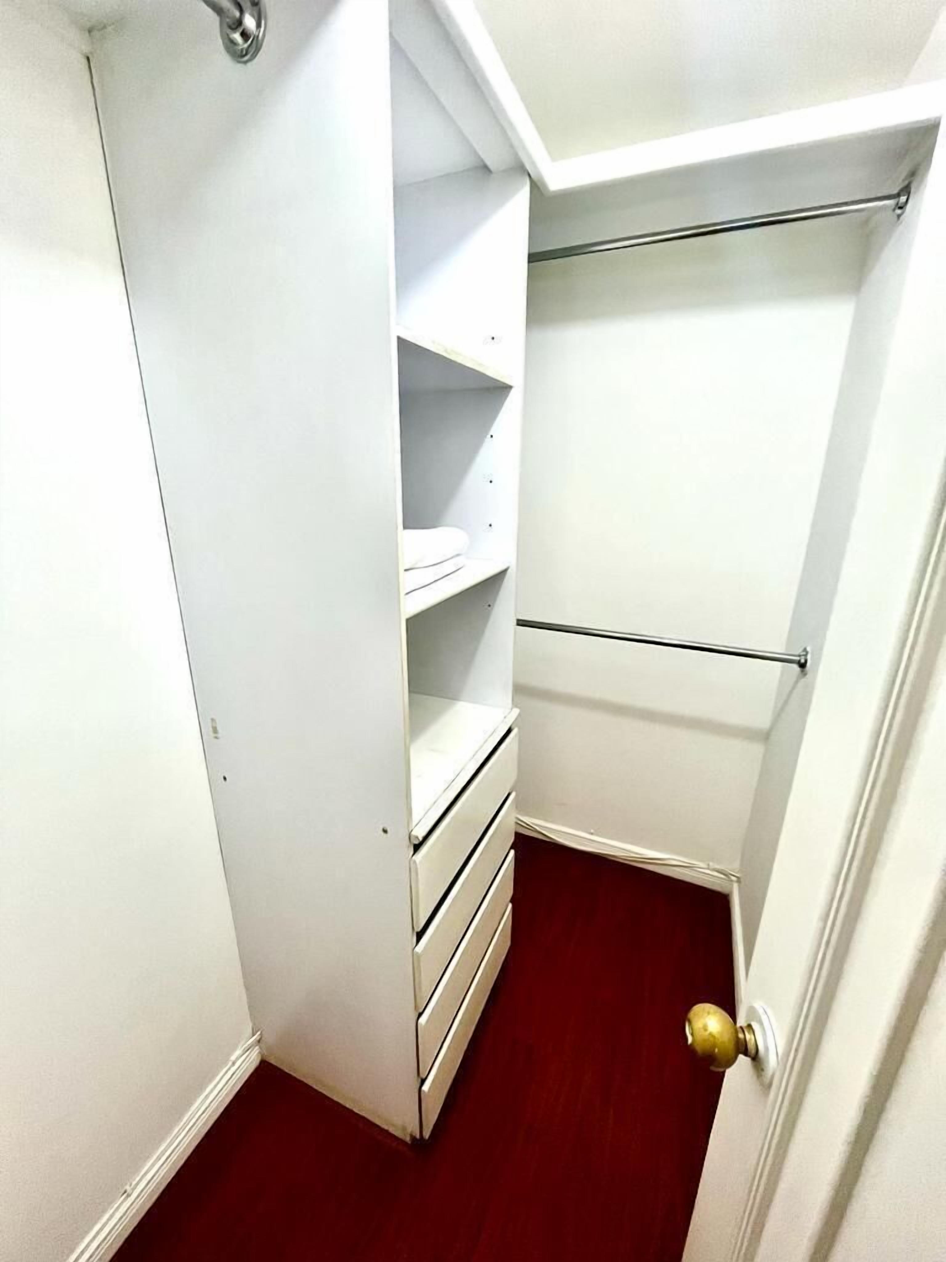 A walk-in closet with open shelves and drawers, a metal rod for hanging items, and a red carpeted floor.