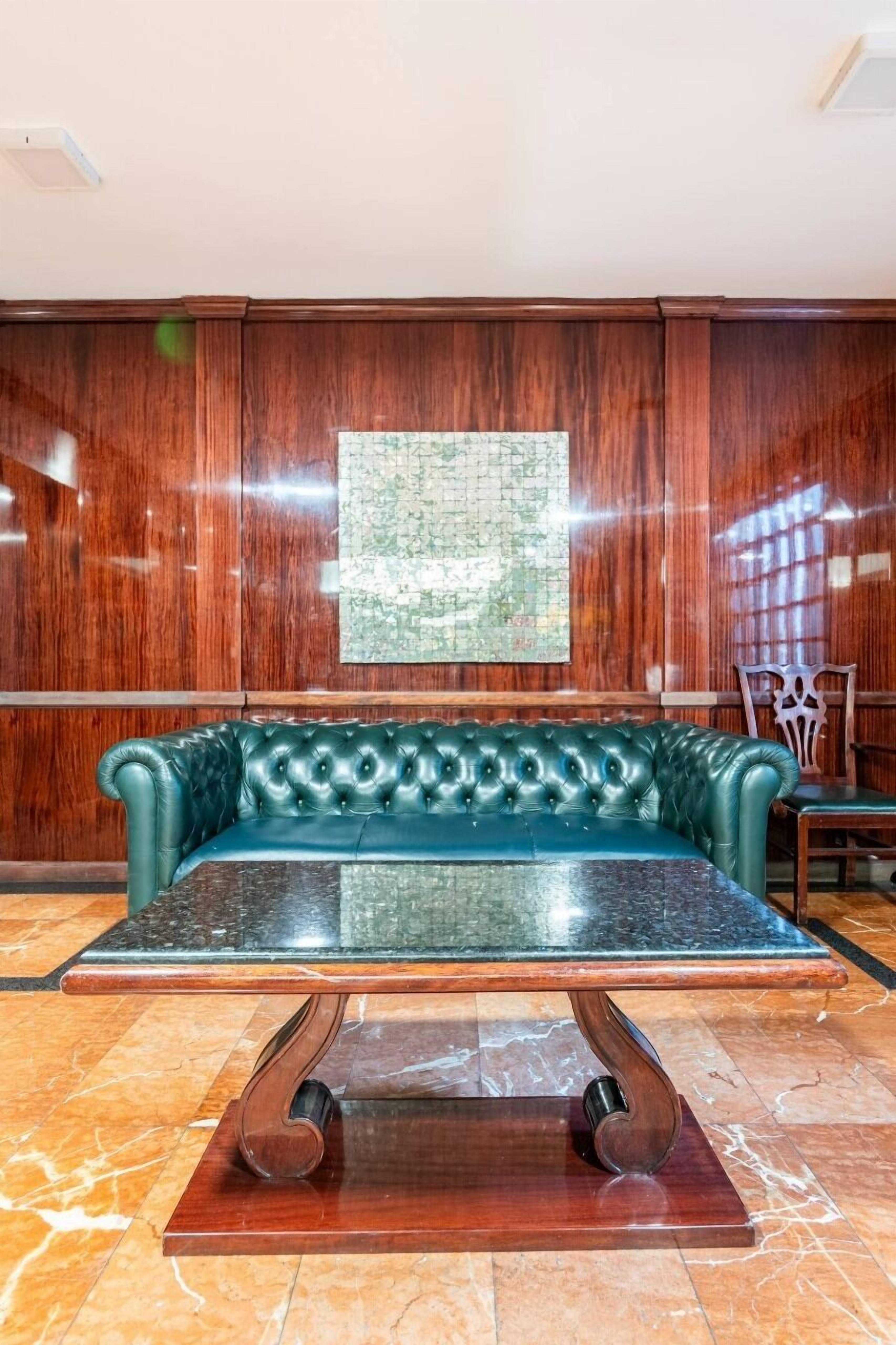 A green leather sofa with a marble table in front, wooden panel walls, and a map on the wall.