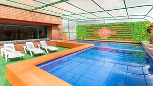 An indoor pool area with a glass ceiling, a brick wall with a green vertical garden, and white lounge chairs. - Fontana Suites (Quito)