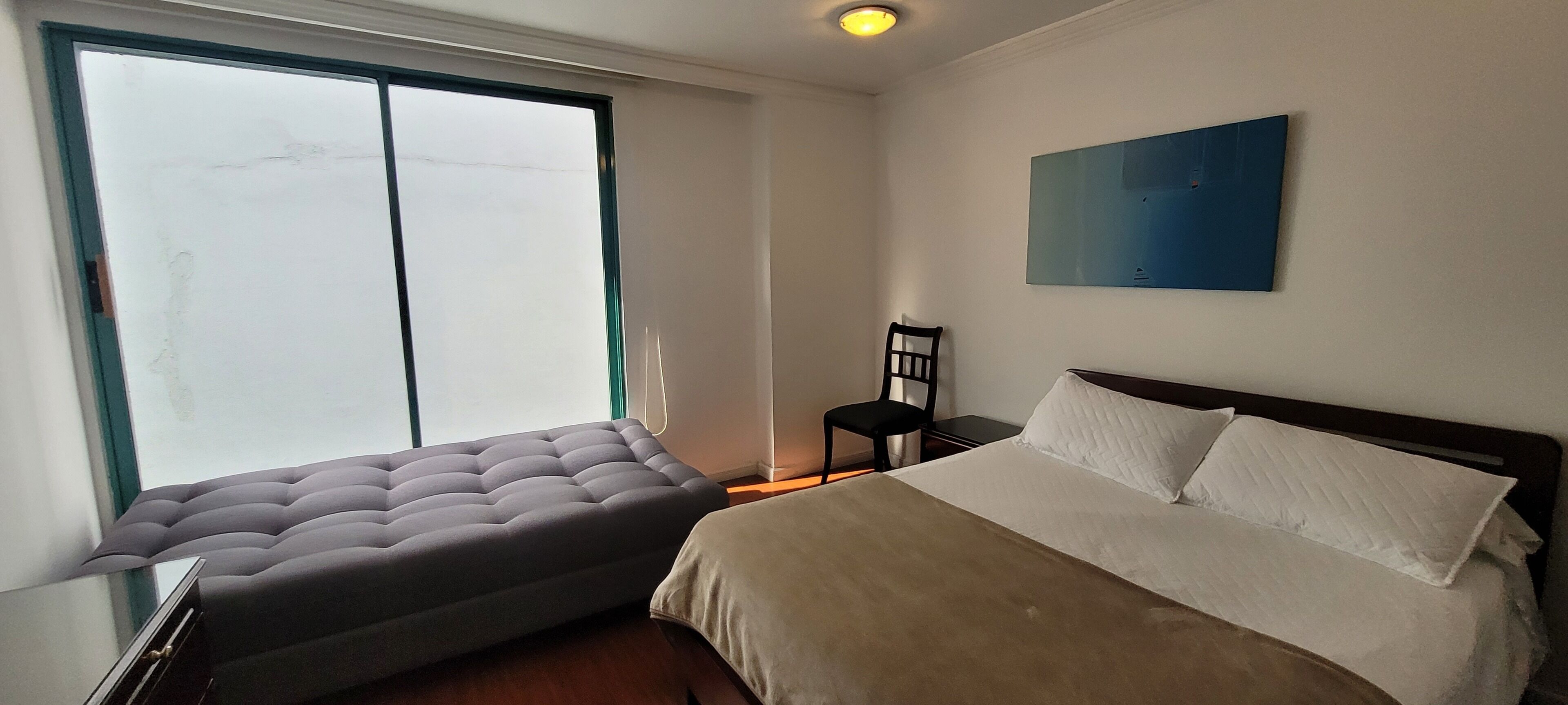 A bedroom with a bed, a window, a chair, and a painting on the wall.