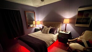A hotel room with a bed, two bedside tables, a chair, a mirror, and a red carpet. - Practical Zen: 4-bedroom 5-bed 2-bath close to everything, flexible, cookies. (Lawrence)