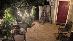 A patio area with a round table and chairs, a small fountain, and a red door. - Practical Zen: 4-bedroom 5-bed 2-bath close to everything, flexible, cookies. (Lawrence)