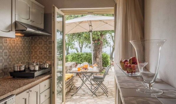 A kitchen with a dining area visible through an open door, featuring a table set for breakfast with fruit and a glass.