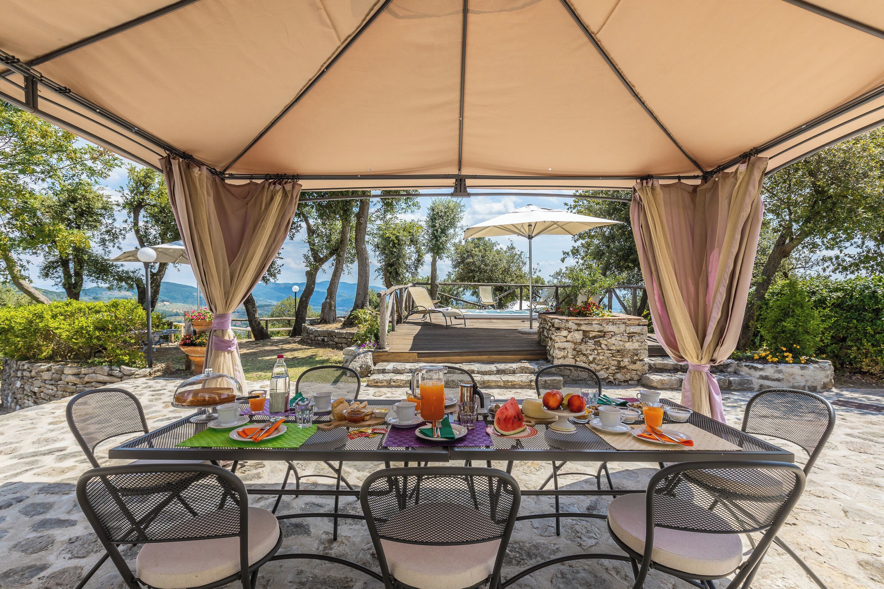 Un espace de restauration en plein air avec une table dressée pour le petit-déjeuner, offrant une vue sur une piscine et un paysage pittoresque.