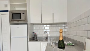 A modern kitchen with white cabinets, a microwave, a sink, and a bottle of champagne. - Panoramic sea views, sunny, private balcony, refurbished on Atalaya Complex (Tías)