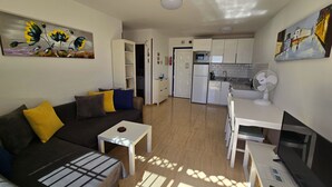 A modern living room with a sofa, a coffee table, and a TV. There is a kitchen area with a microwave, refrigerator, and sink. - Panoramic sea views, sunny, private balcony, refurbished on Atalaya Complex (Tías)