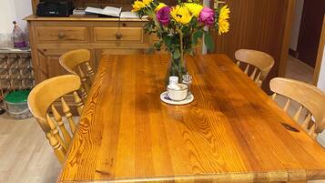 Une table à manger en bois, avec des chaises, un vase rempli de fleurs et une bibliothèque contenant des livres et des objets décoratifs.