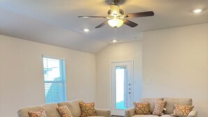 Ein geräumiges Wohnzimmer mit zwei beigefarbenen Sofas, gemusterten Zierkissen, einem Deckenventilator und Holzboden.