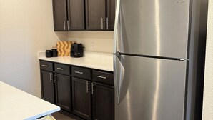 Eine Küche mit dunklen Holzausführungen, einem Edelstahl-Kühlschrank und einer weißen Arbeitsplatte.