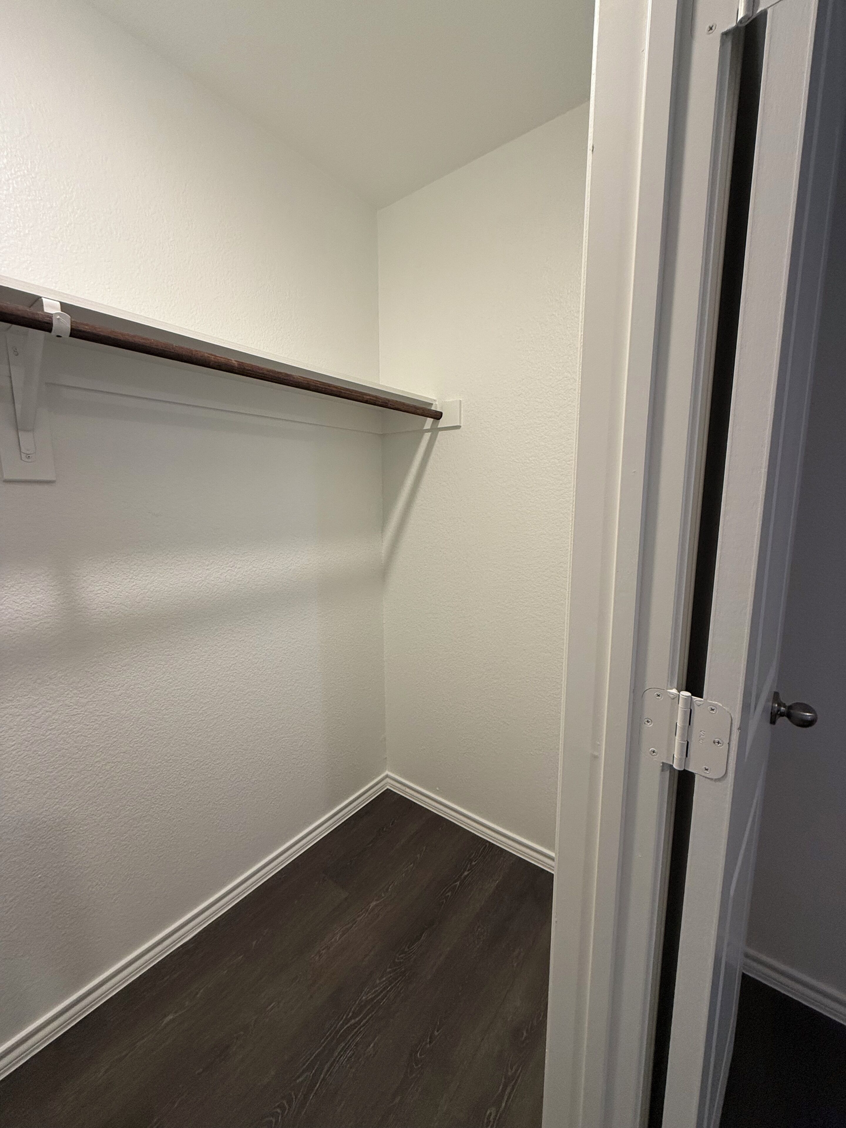 A small, narrow closet with a wooden rod and a white door.