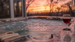 Een jacuzzi met een glas rode wijn, een houten terras en een huis op de achtergrond.