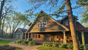 Een tweelaags huis met een opvallende puntgevel, een veranda en een aangelegde tuin met boomstammen.