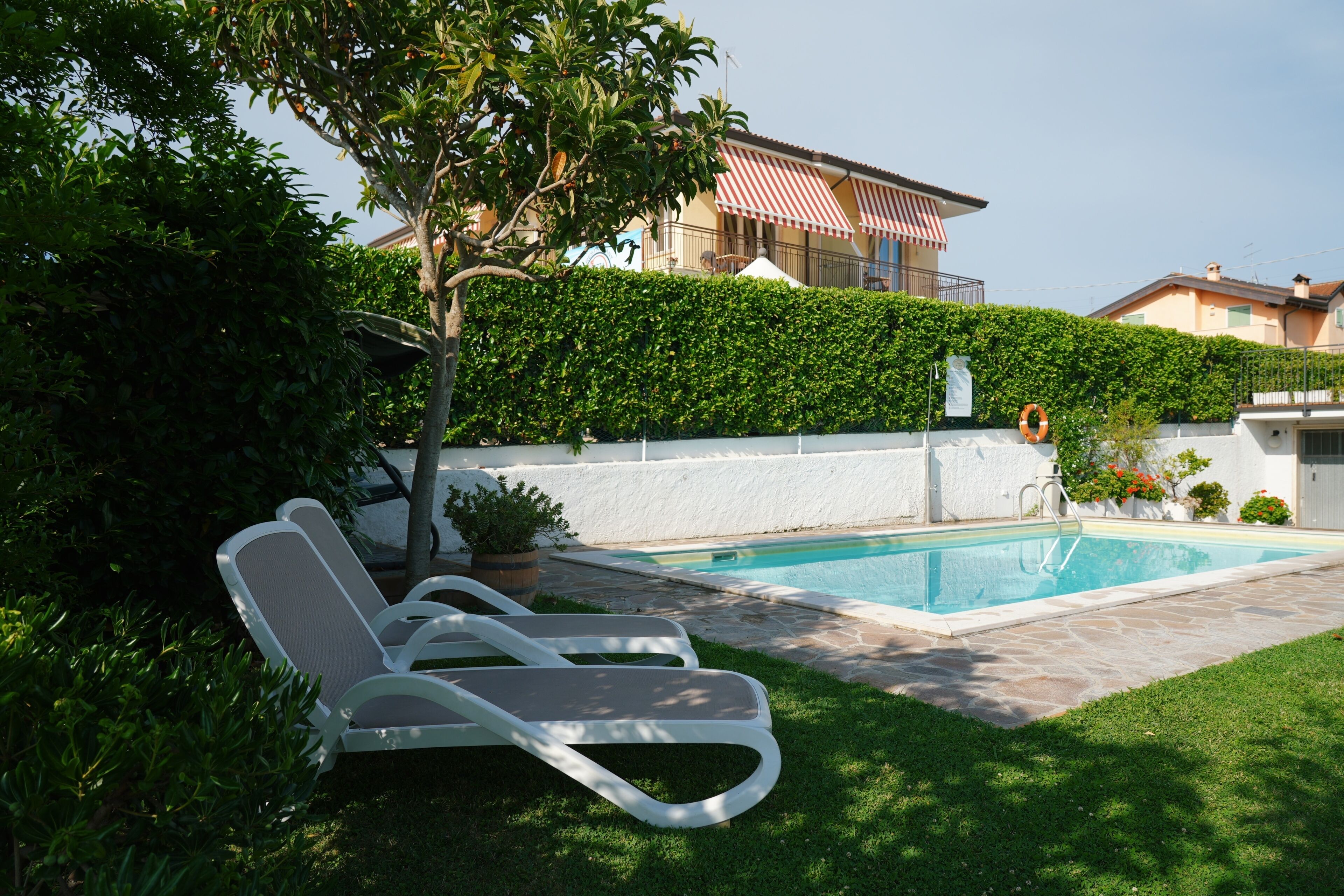 Ein Pool mit Liegestühlen, einer Hecke und einem Gebäude im Hintergrund.