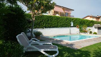 Ein Pool mit Liegestühlen, einer Hecke und einem Gebäude im Hintergrund.