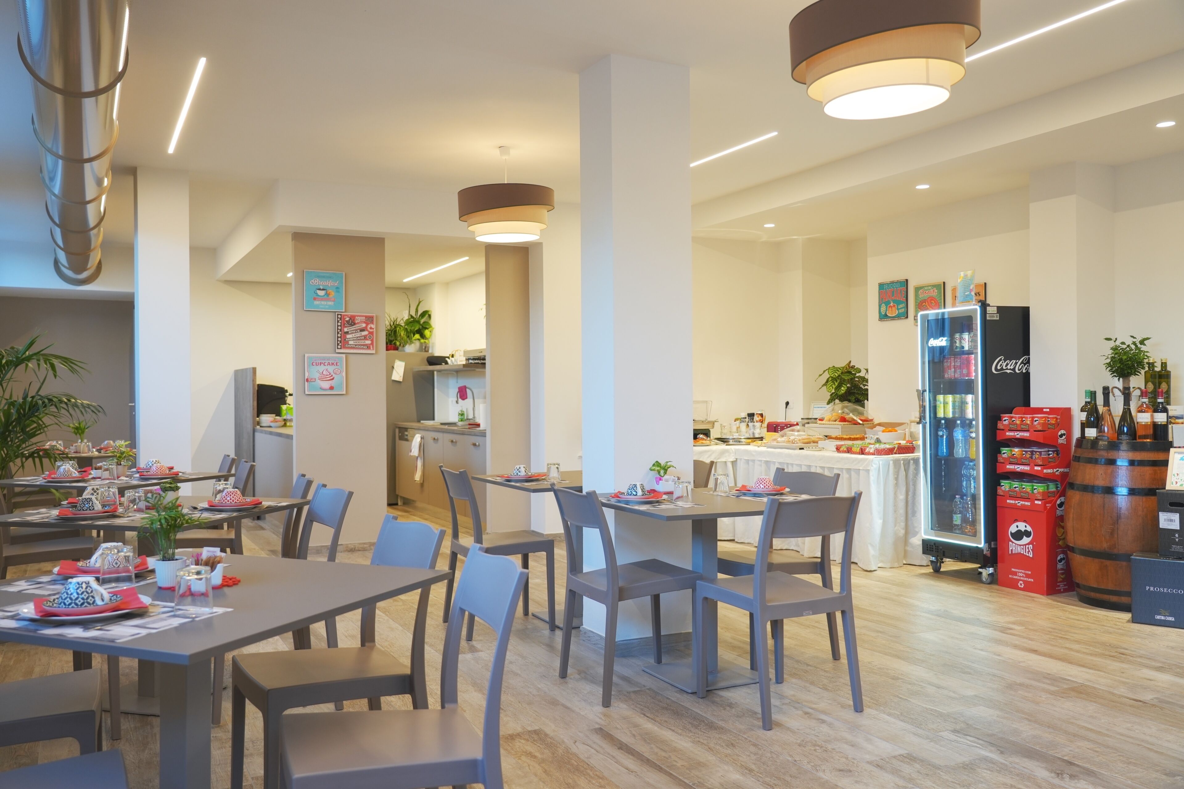 Un espace repas moderne avec des tables et des chaises, une cuisine en arrière-plan et un réfrigérateur rempli de boissons.