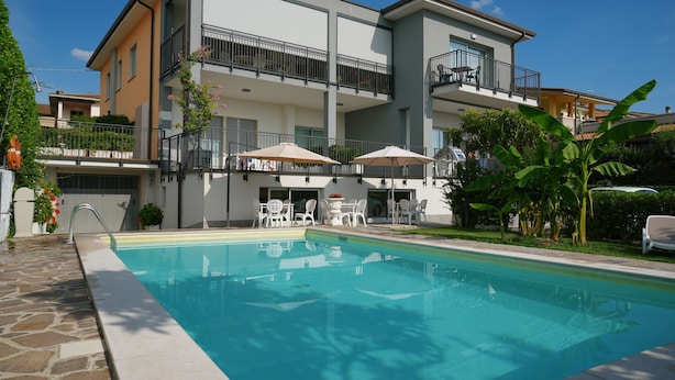A modern two-story building with a swimming pool, outdoor seating, and a balcony.