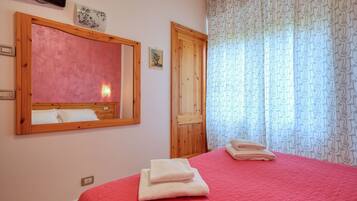 Un dormitorio con colcha roja, cabecera de madera, un espejo grande y una puerta con marco de madera.