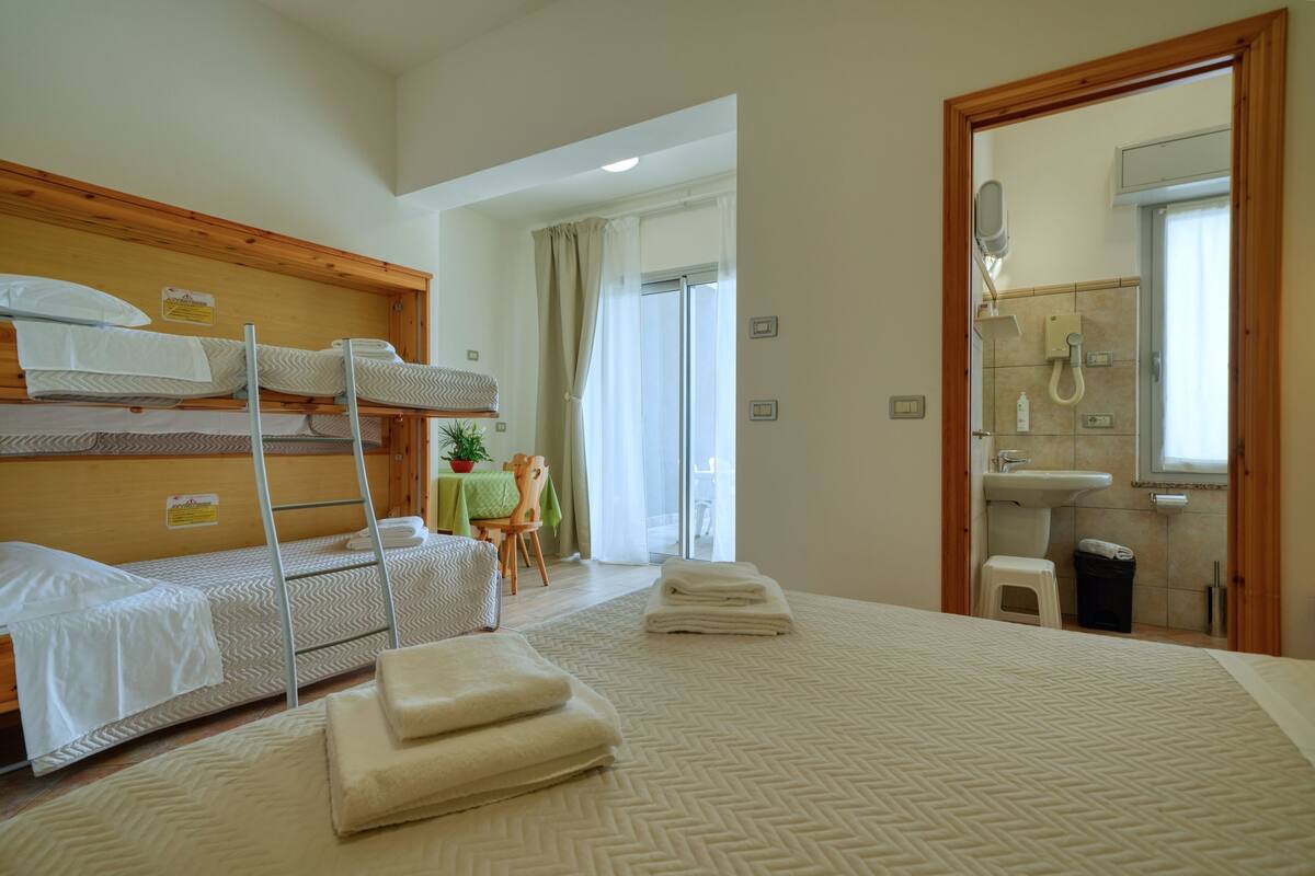 A hotel room with bunk beds, a bathroom with a sink and mirror, and a view of the outside.