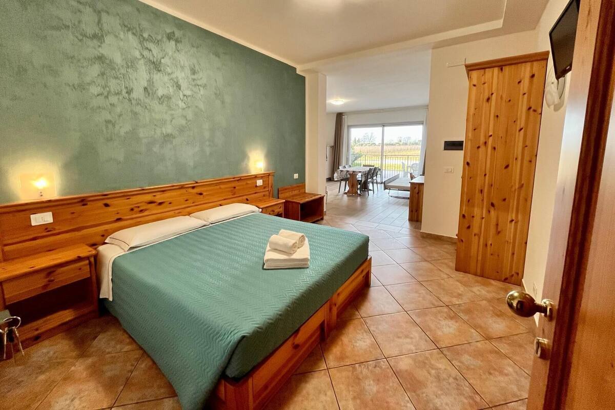 A hotel room with a large bed, wooden headboard, and a view of the outdoor area.