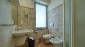 A bathroom with a sink, toilet, bidet, and a window with a curtain.